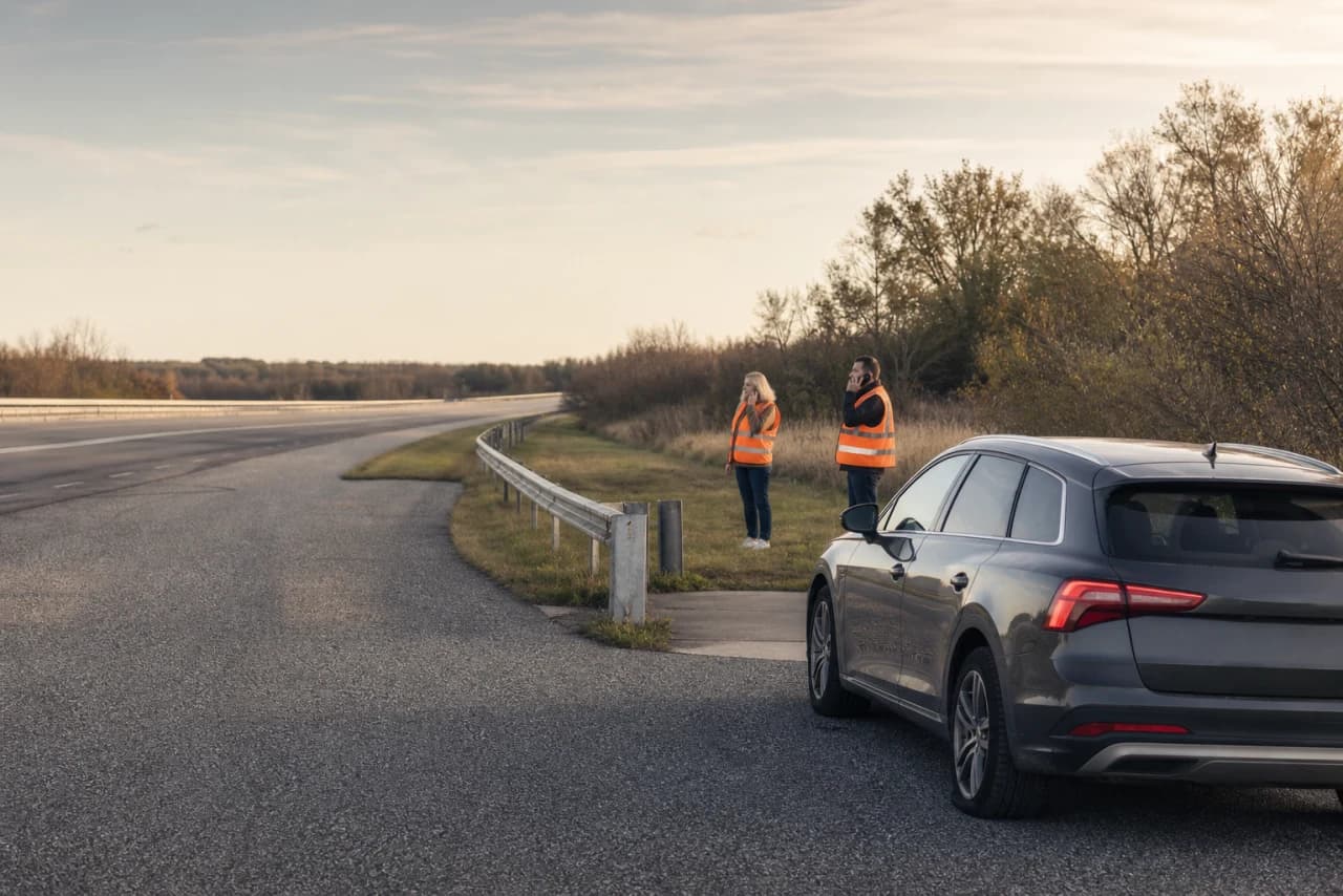 Bil med punkteret dæk holder sikkert væk fra kørebanen mens passagererne står bag autoværnet