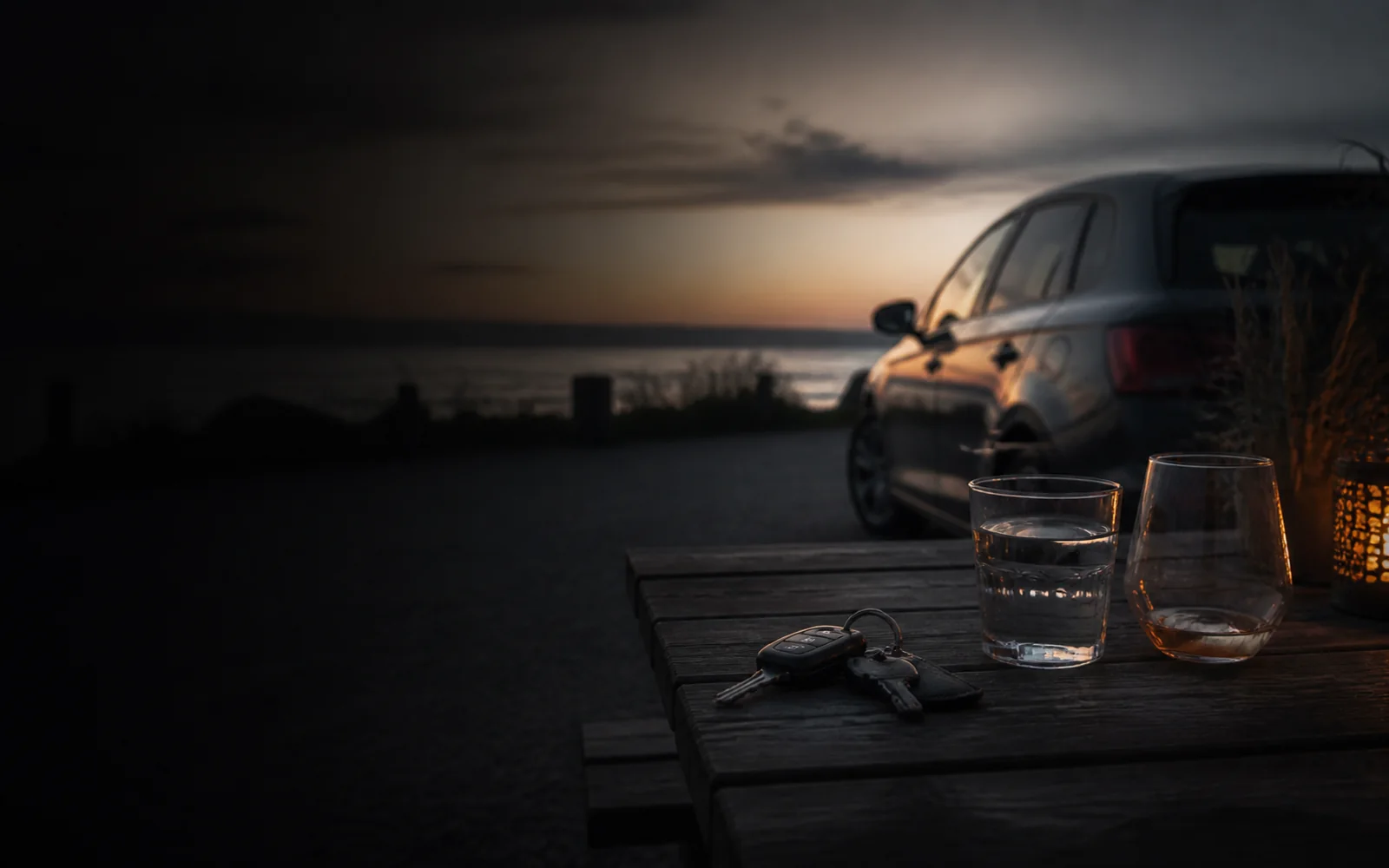 Bilnøgler ligger ved vand og et vinglas, mens bilen holder parkeret